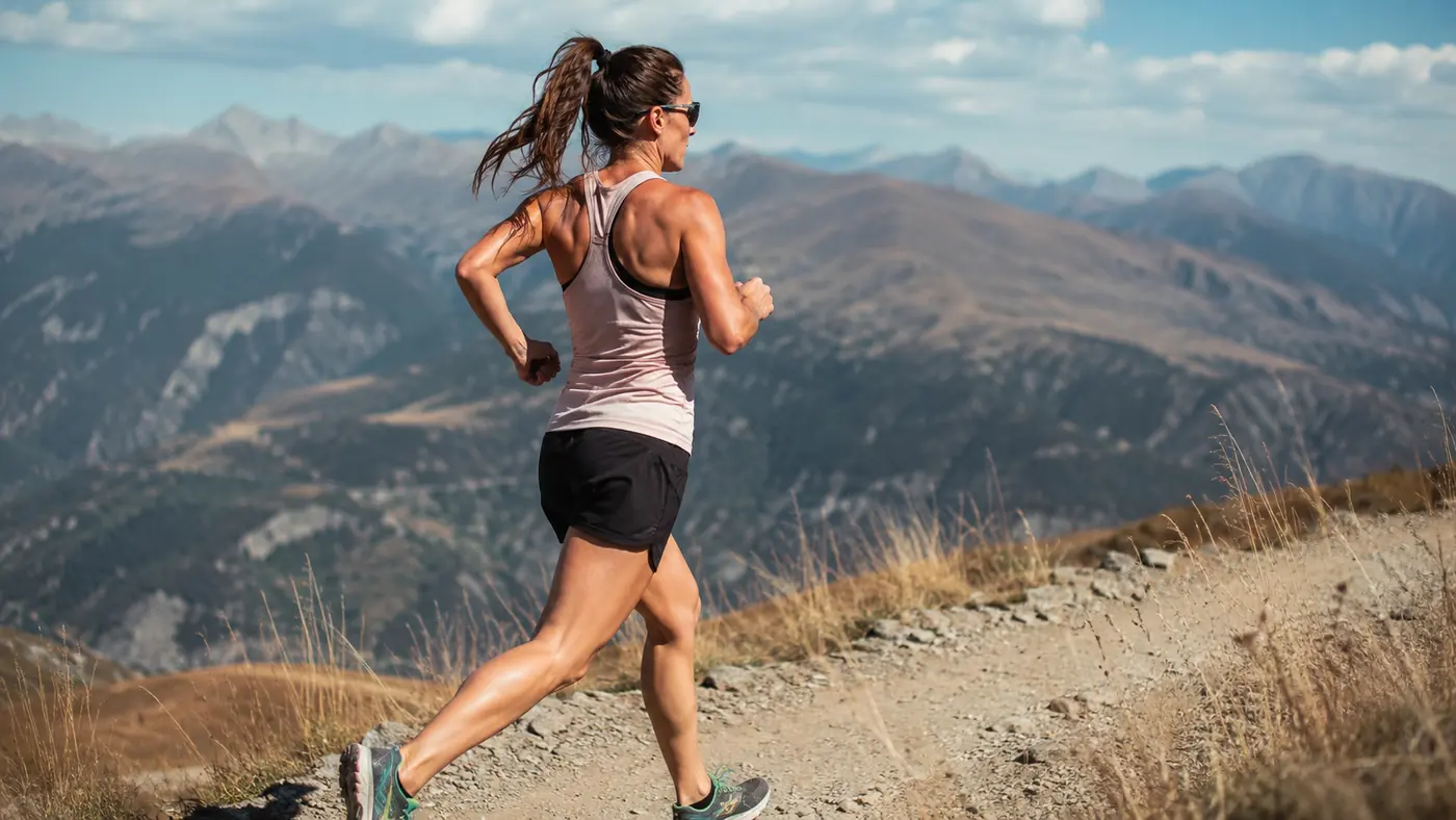 A runner mid-stride on a dry, high-altitude trail with visible torso rotation and relaxed arm swing