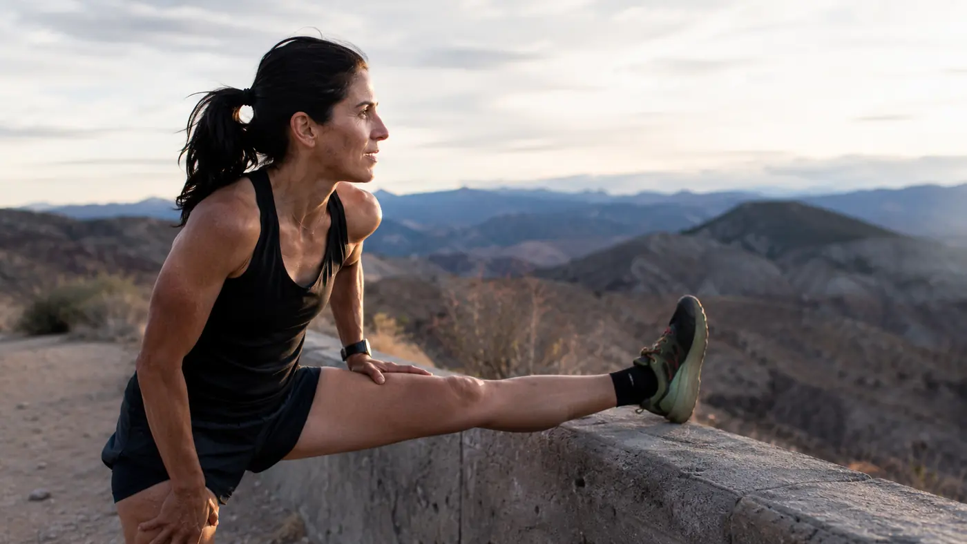 Runner stretching a calf against a low wall on a dry, high-altitude trail after a run