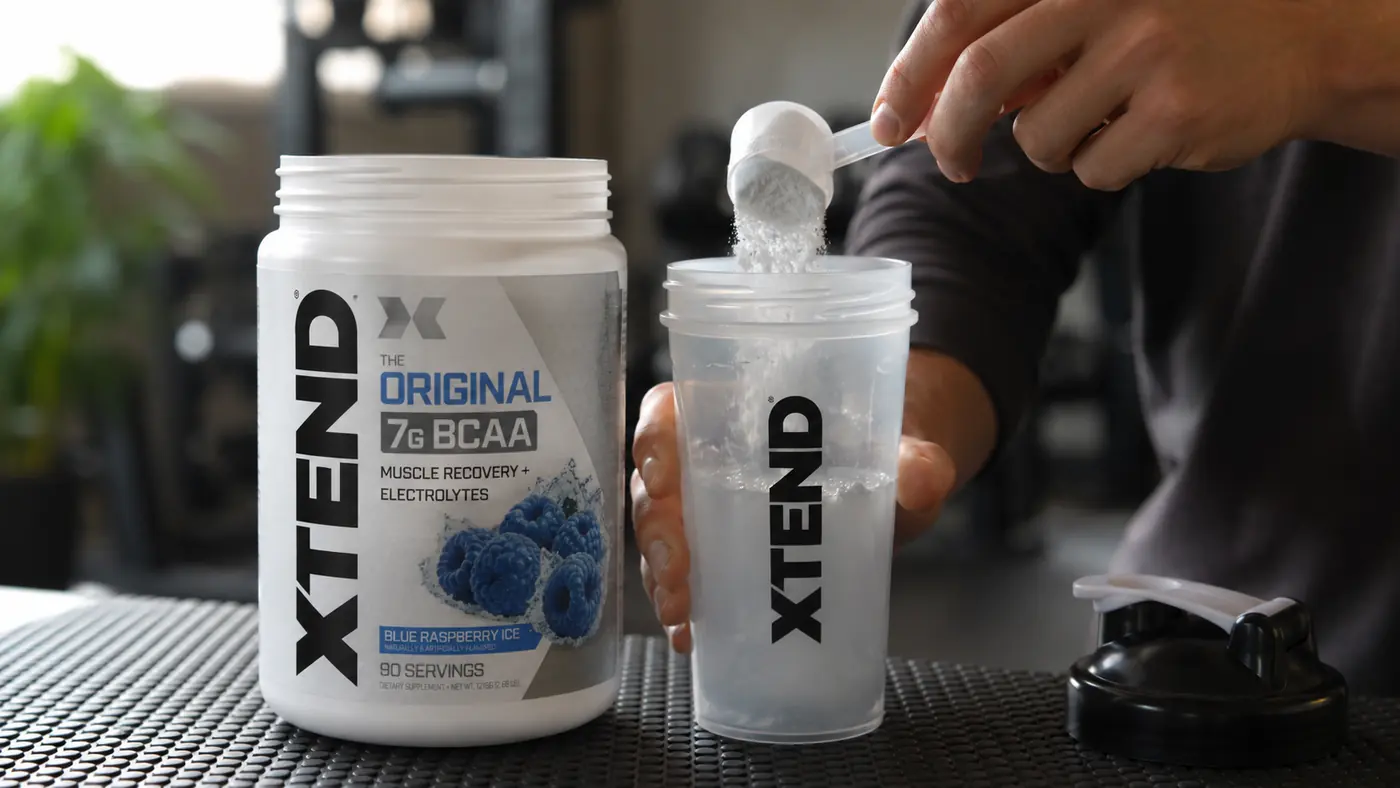 Hands mixing blue raspberry BCAA powder into a shaker bottle before a lifting session
