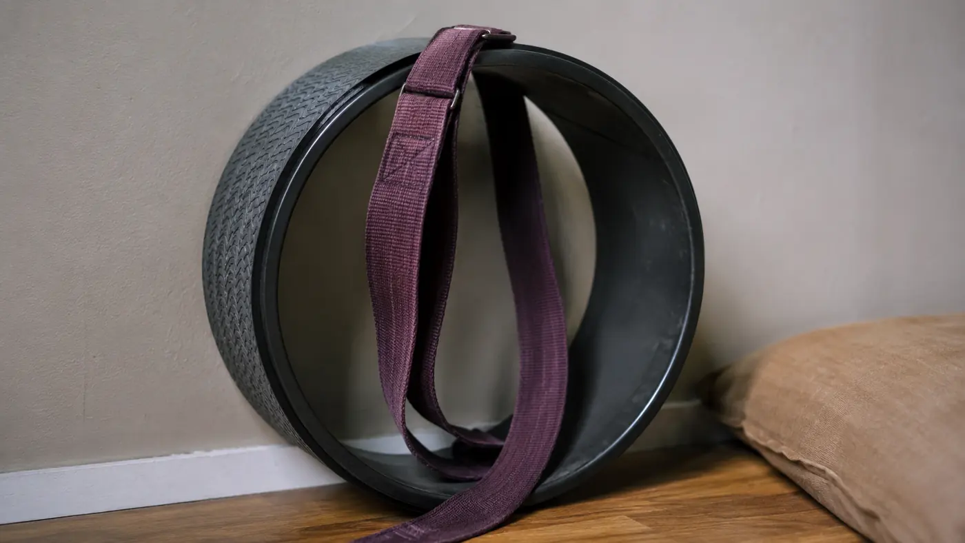 A strap looped through a yoga wheel resting against a wall, showing wear at the stitching after months of use